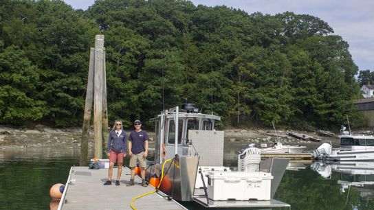 The Island Institute’s Lia Morris (left) is working with Willy Leathers (right) and his crew at Maine Ocean Farms to collect performance data on the electric boat Heron, pictured here charging from a low-capacity shoreside power supply at a slip in South Freeport, Maine.